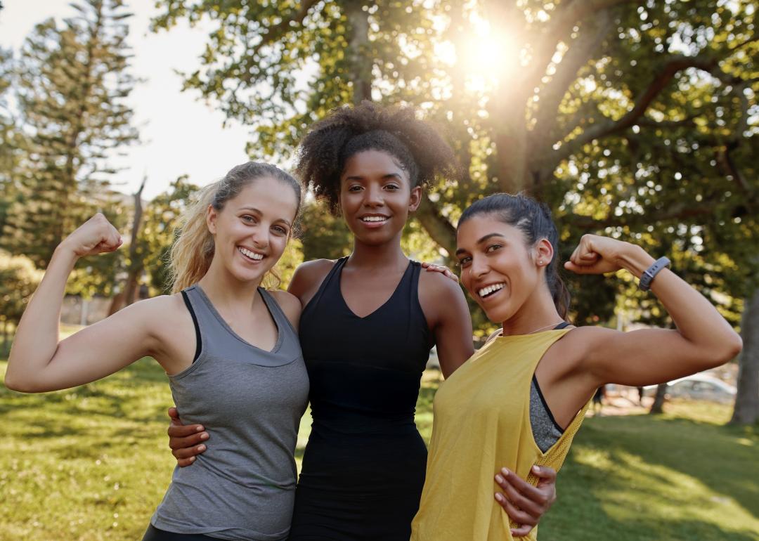 Three women flexing their muscles in a park.
