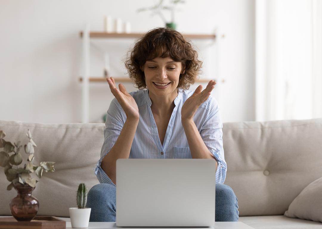 A happy woman sitting on her couch reading good news on her laptop.