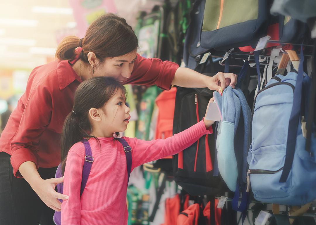 A mother helps her young daughter to pick a new bag for school at a store.