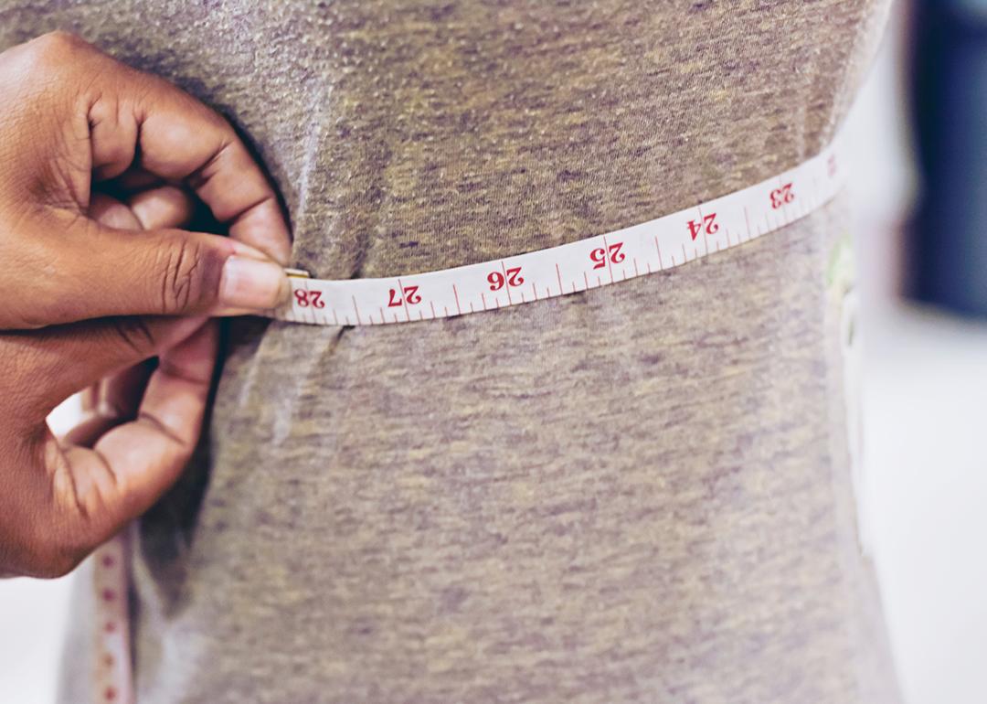 A tailor taking measurements of a client's torso with a tape measure.