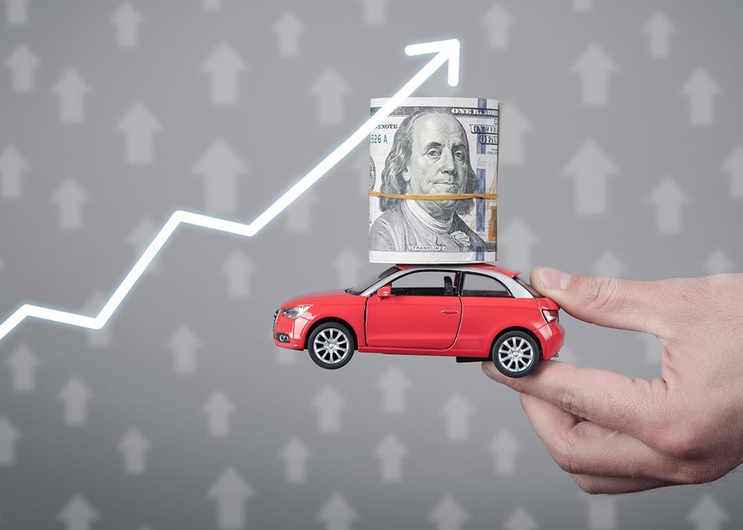 A miniature car with a dollar on top held up with an upward arrow as a concept of rising prices.