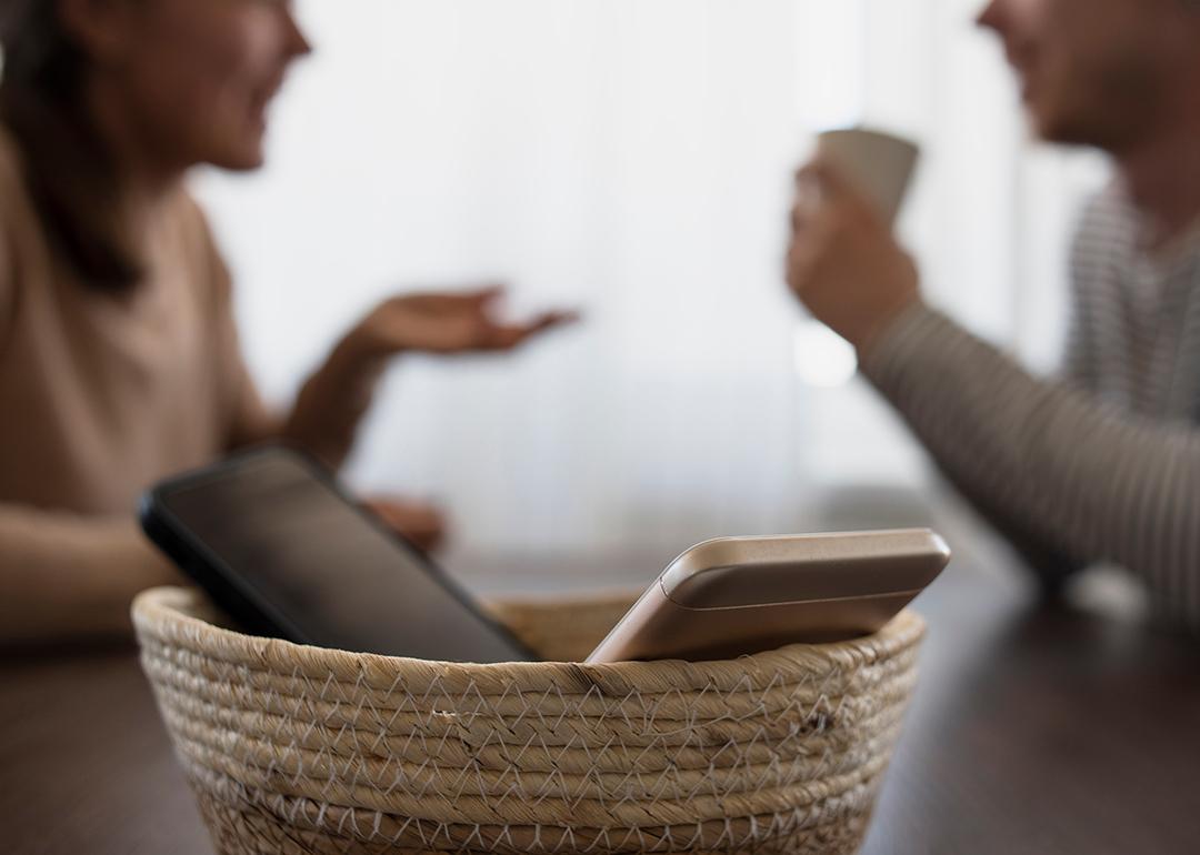Two phones in a basket with two people catching up in the background.