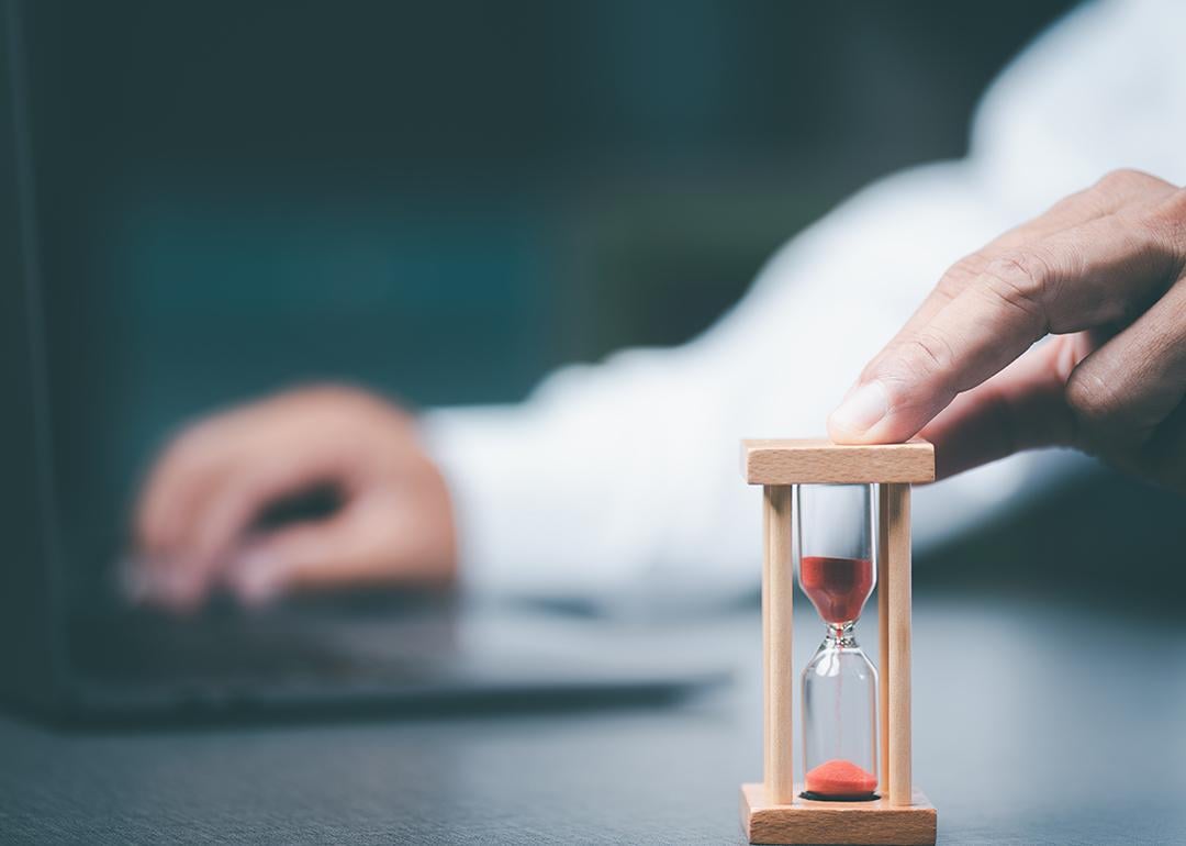 A business employee using a small time hourglass beside a laptop.