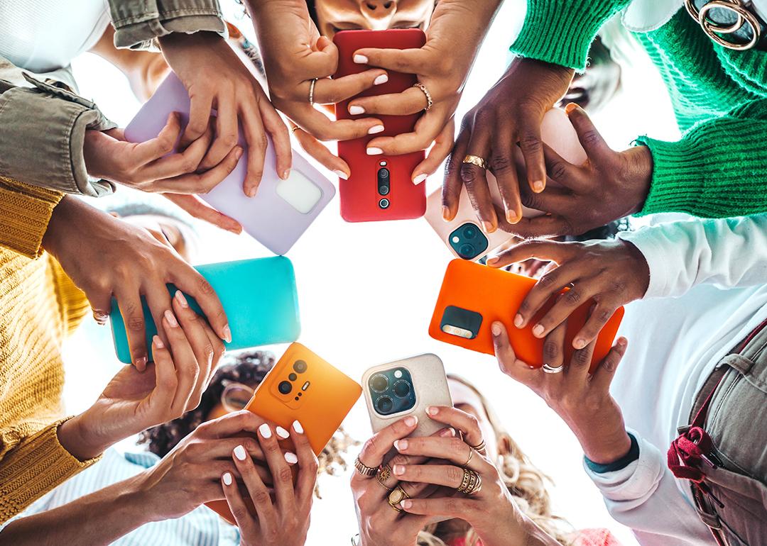 A group of young people using their smartphones outside while forming a circle.