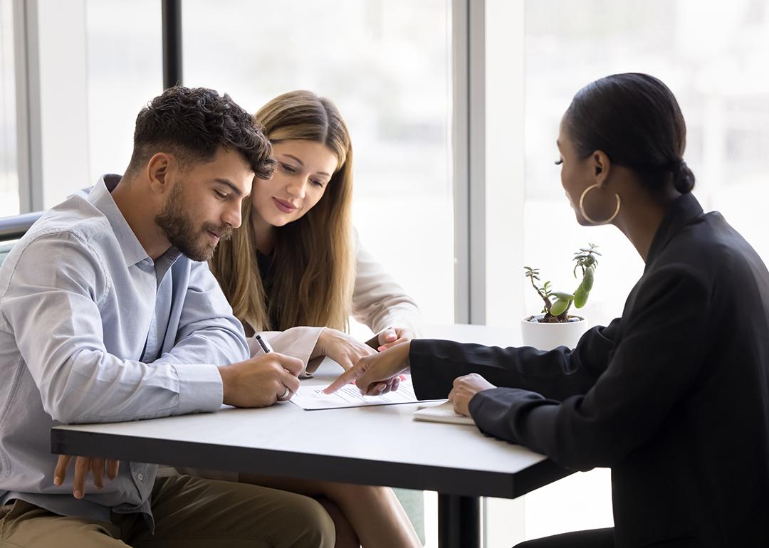 A realtor guiding a couple on signing a property contract.