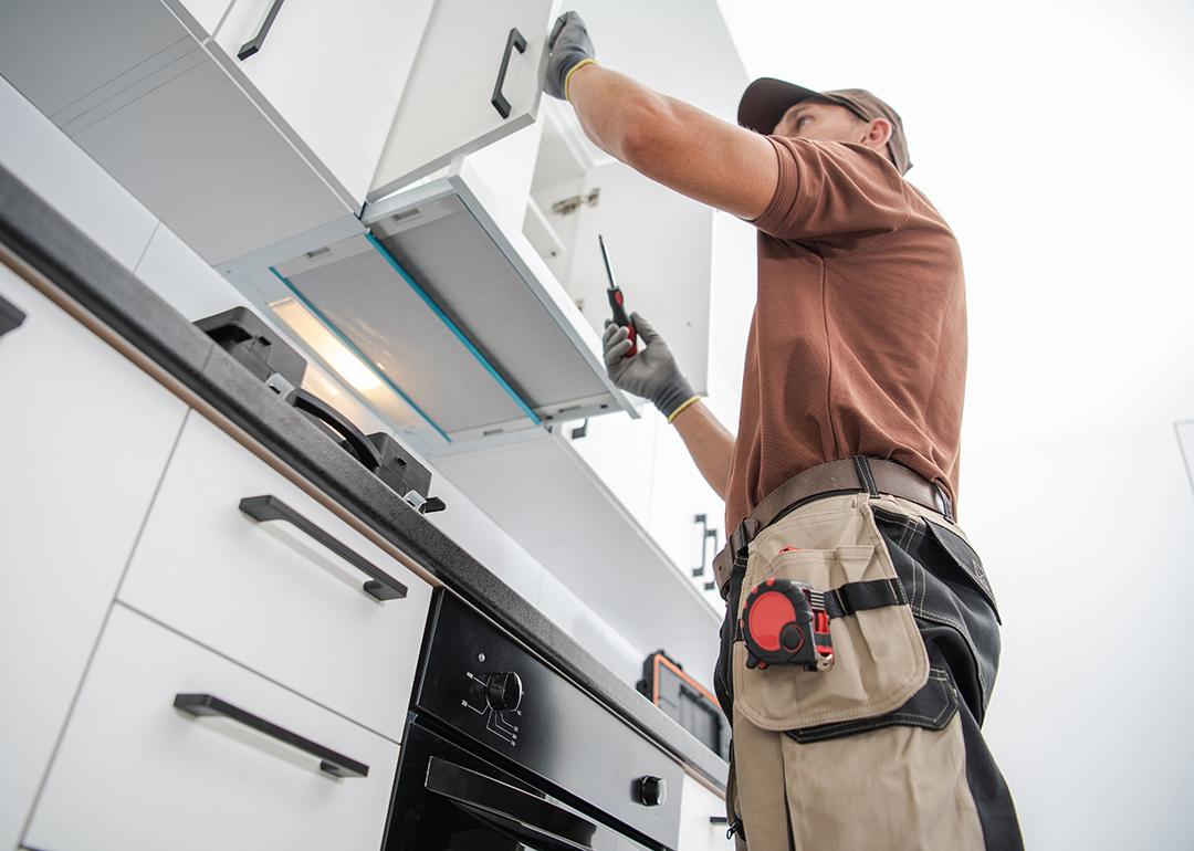 A cabinetmaker finishing a white, modern cabinet installation