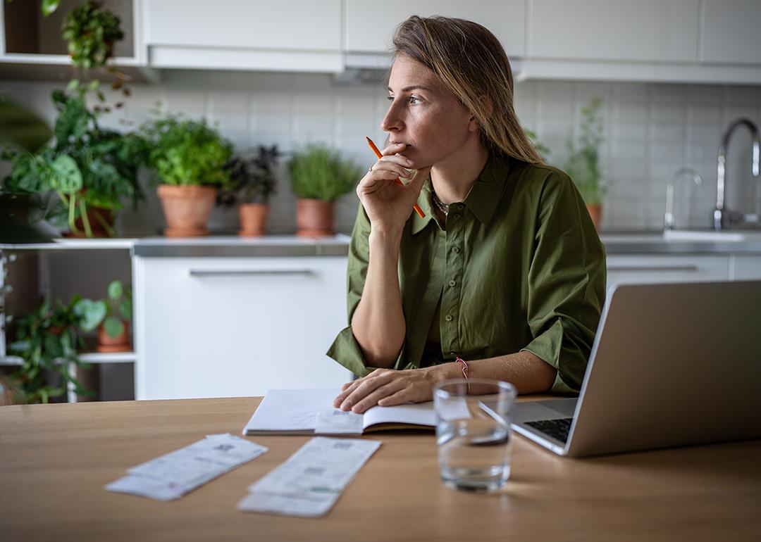 A pensive woman at home working on accounting documents.