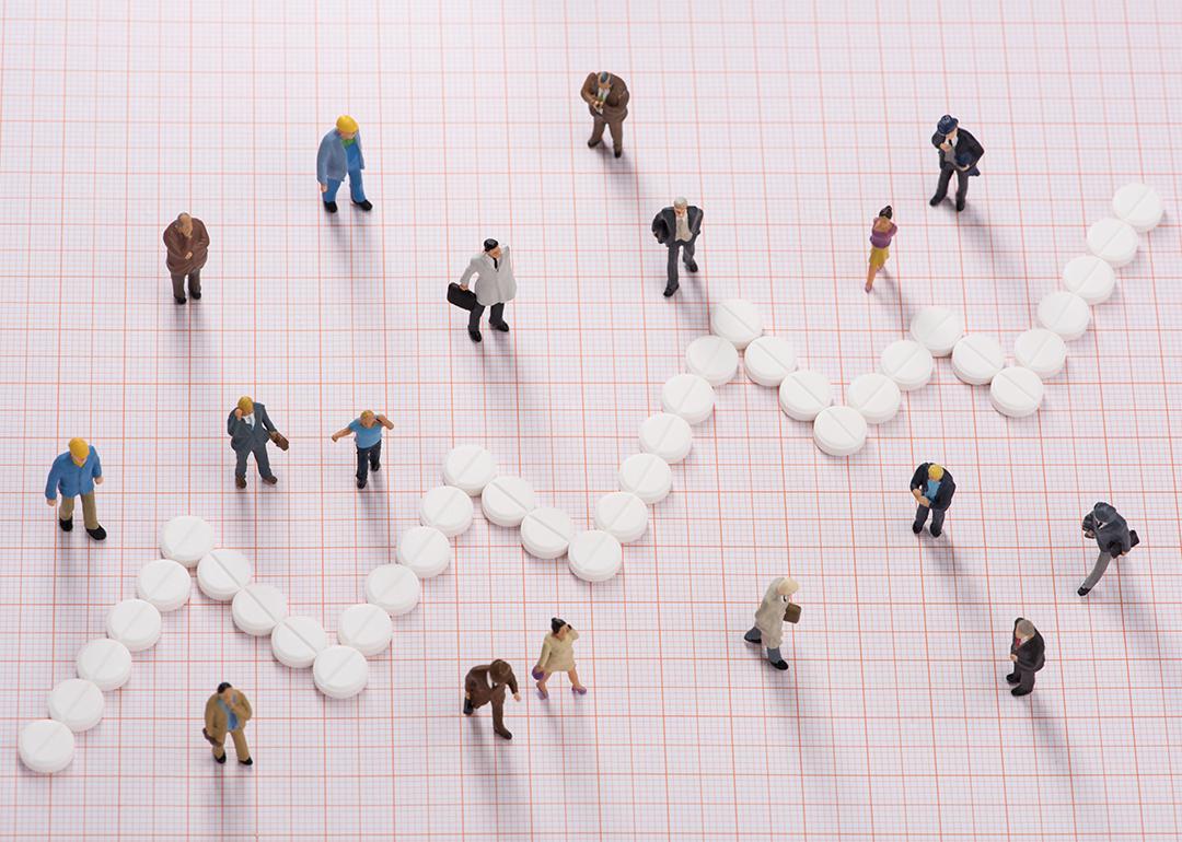 White pills forming a jagged line, dividing small figures of different people to represent different healthcare costs among groups.