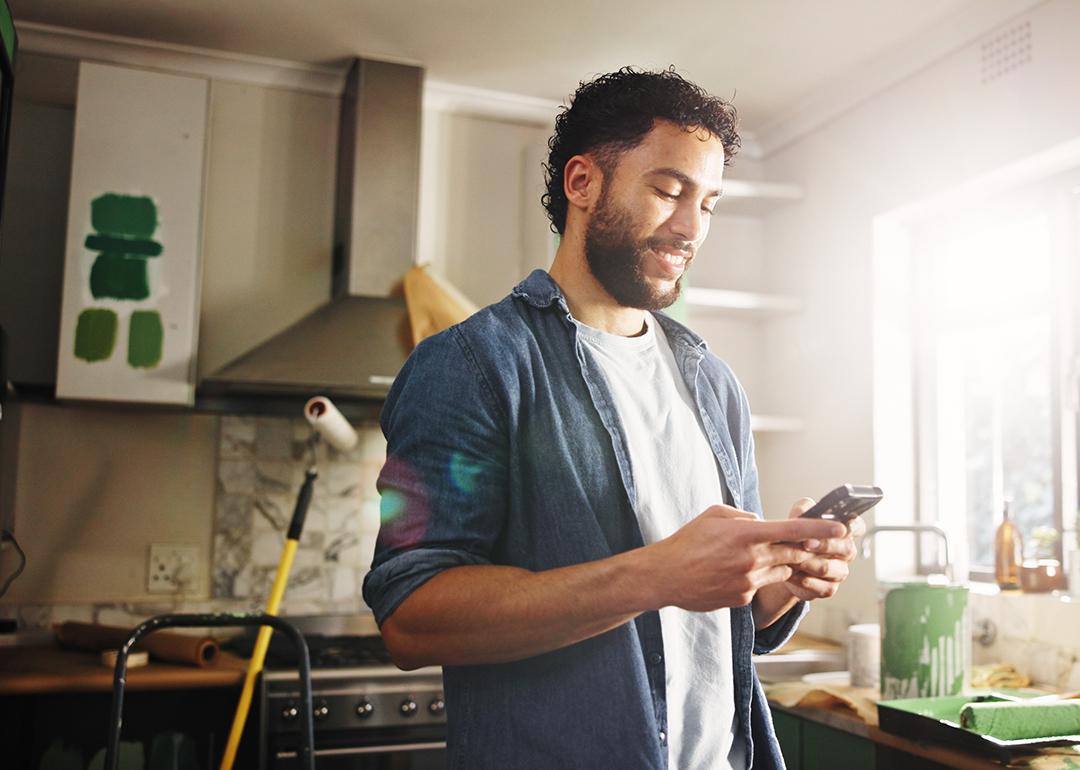A man his apartment's kitchen looking up renovation ideas in his phone.