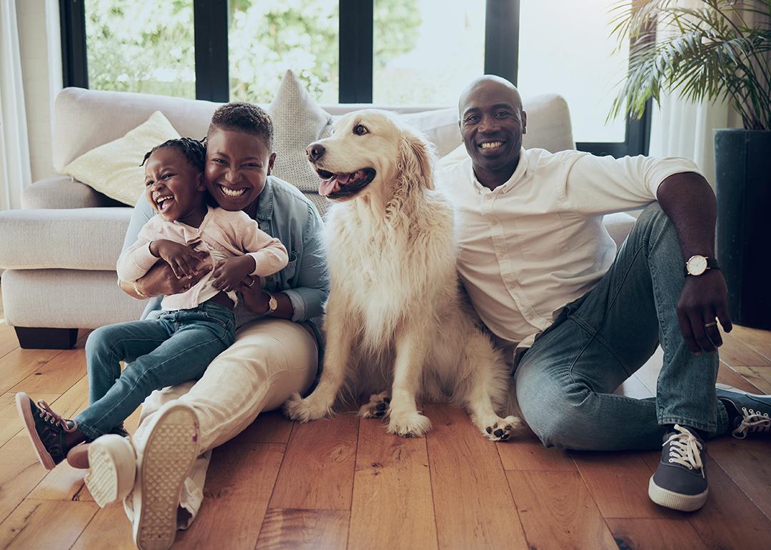 A black family of three and their dog, happily sitting on the living room floor of their home.