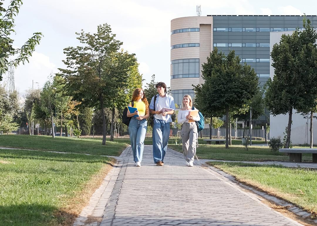 A group of three young college students chatting while walking on university campus footpath.