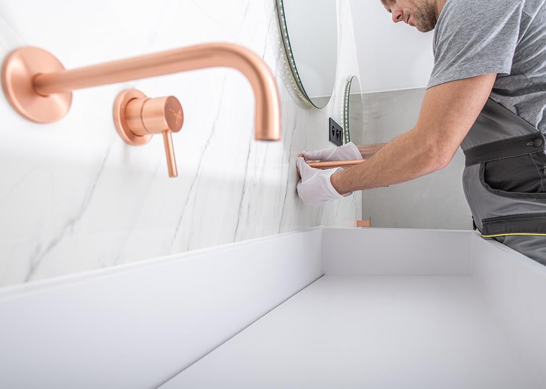 A handyman installs copper faucet to a modern marble wall bathroom.