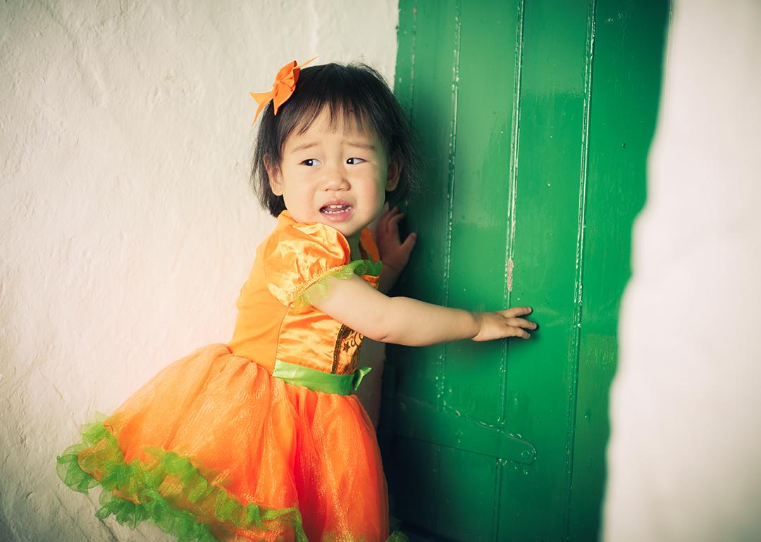 A young girl wearing an orange Halloween dress crying during a party.