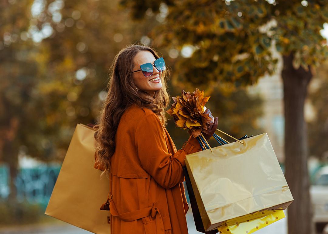 A happy stylish woman holding shopping bags and autumn leaves.
