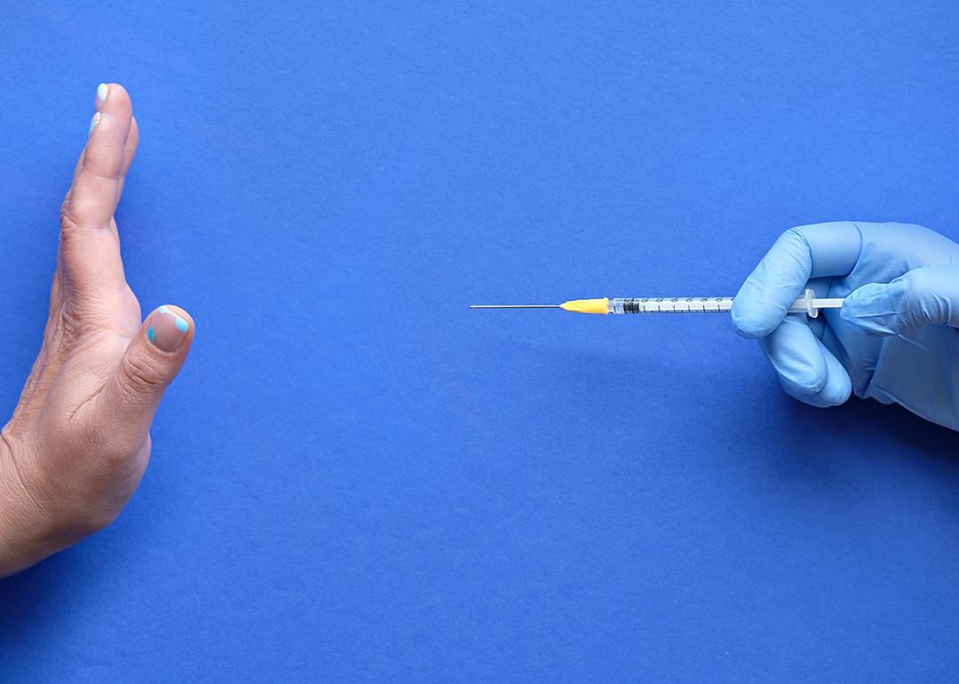 A hand refusing to receive a vaccine syringe.