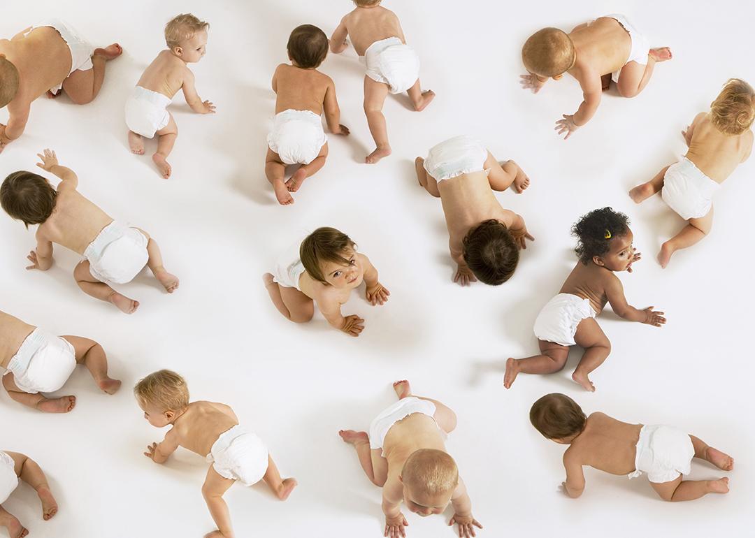 A group of diverse babies crawling on a white floor.