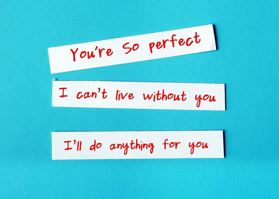 Love bombing messages written on slips of paper such as "I can't live without you," photographed against turquoise background.