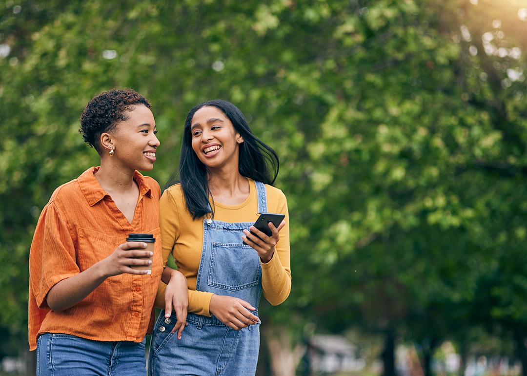 Two women having coffee while walking in a park.