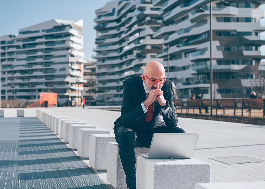 Businessman sitting outdoors and concentrates on his laptop.