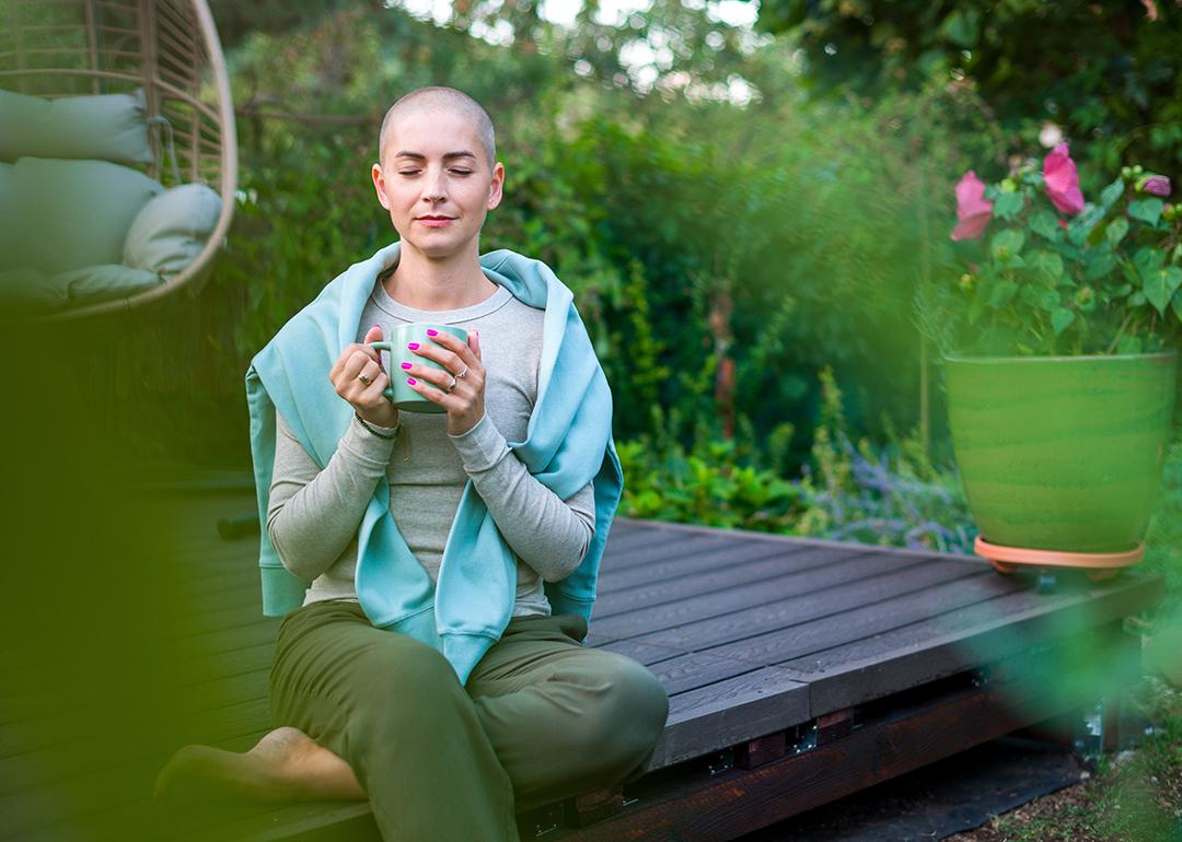 A breast cancer patient sitting on a garden patio with a cup of coffee in her hands.