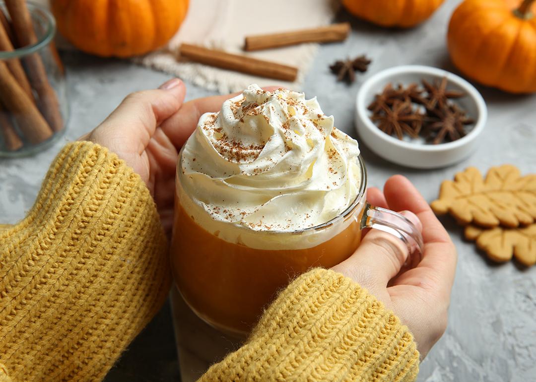 Closeup on a woman holding a cup of pumpkin spice latte with whipped cream.