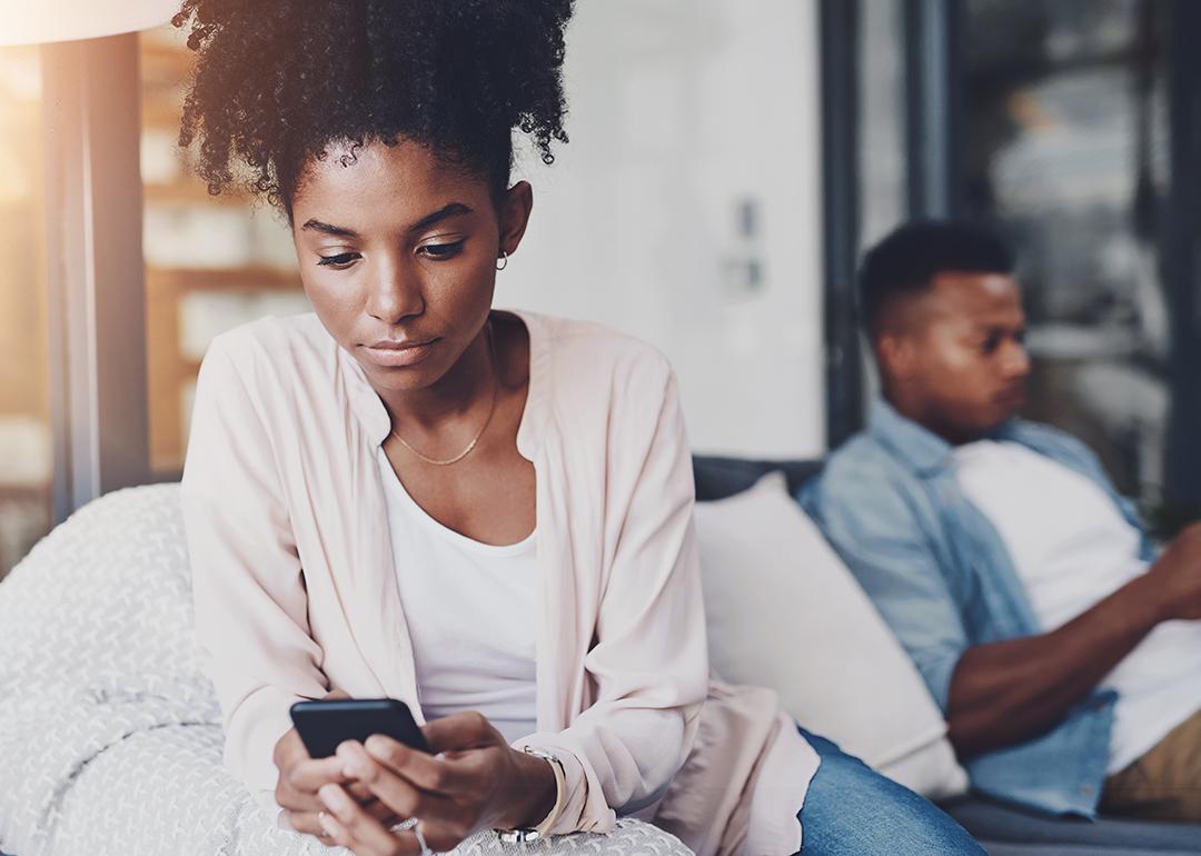 A black couple on their individual phones while sitting apart on the same couch at home.
