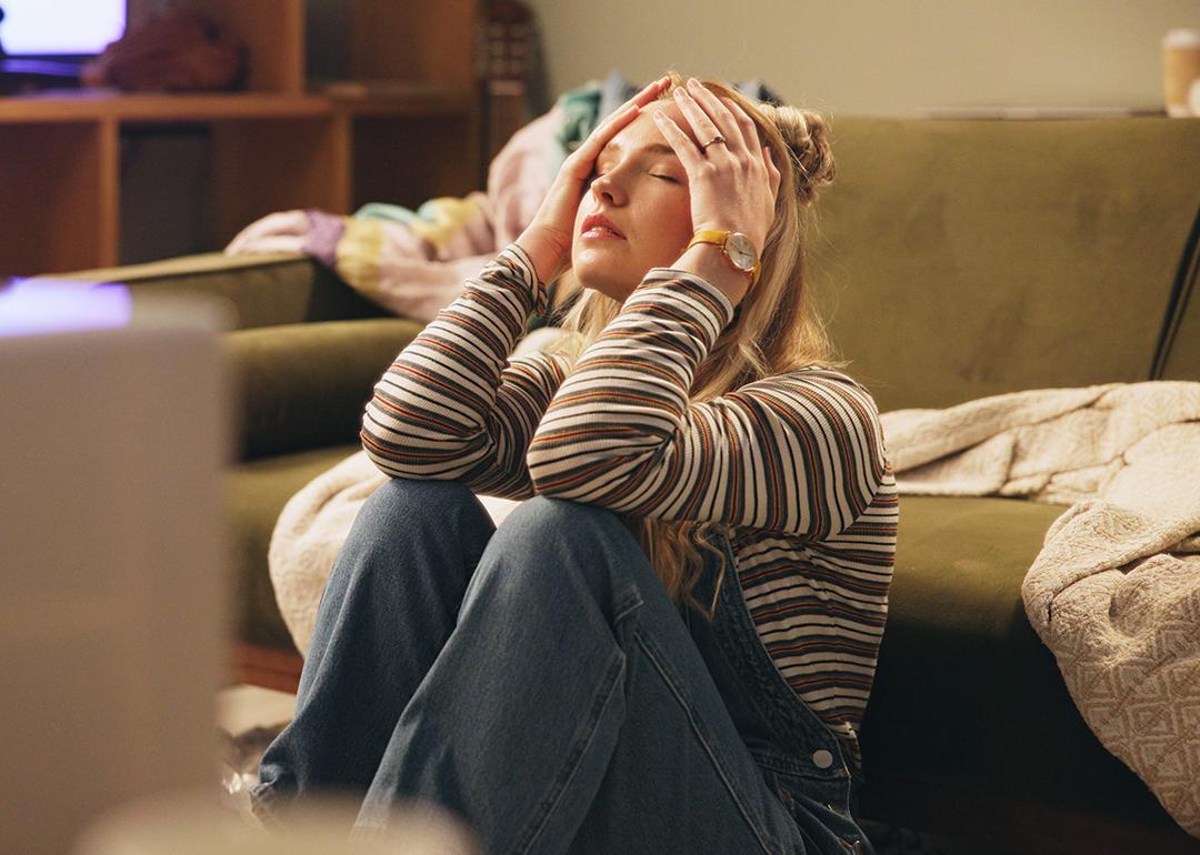 A stressed young woman sitting on the floor holding her head.