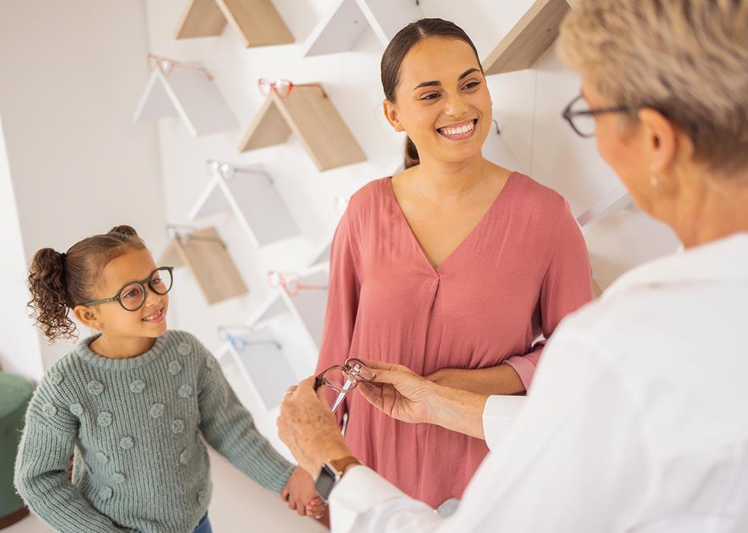 Girl with mother trying on glasses at an eyewear store talking to specialist.