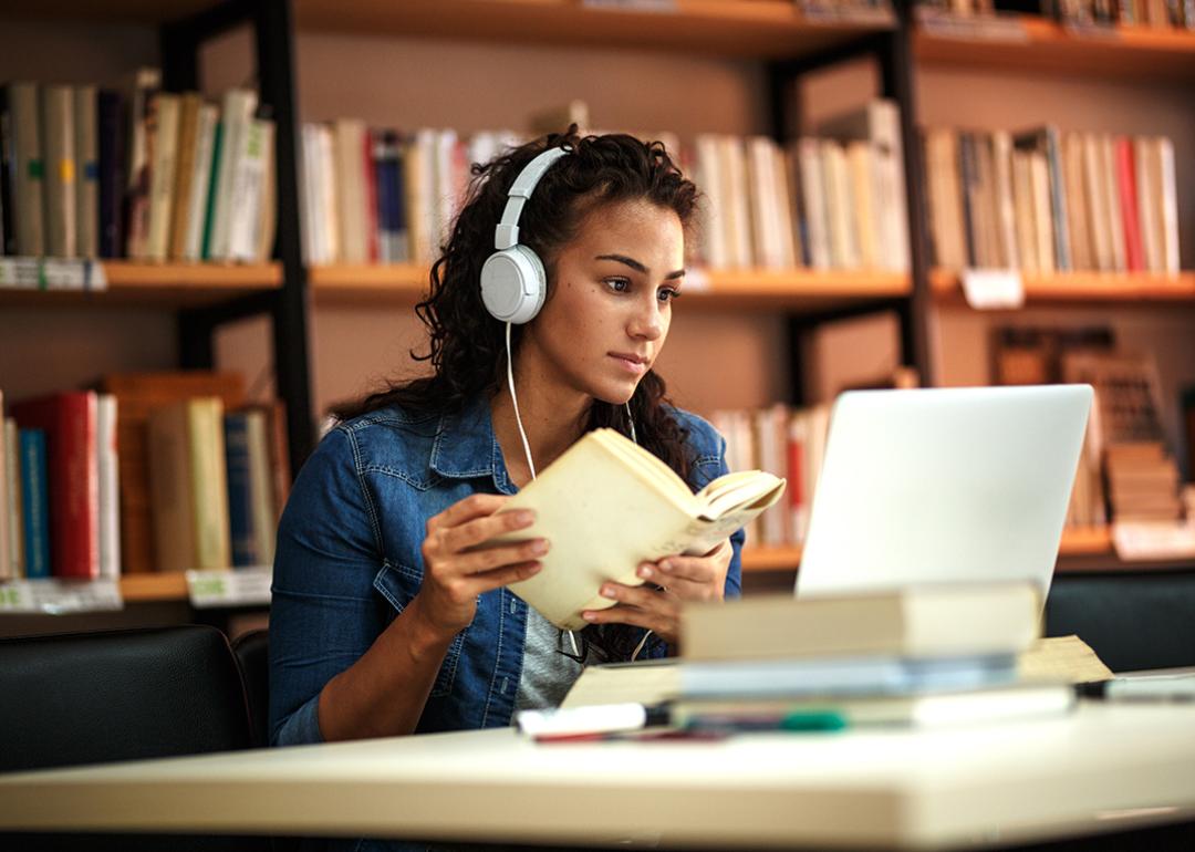 A fema collge student reading a book in a library while listening to music.