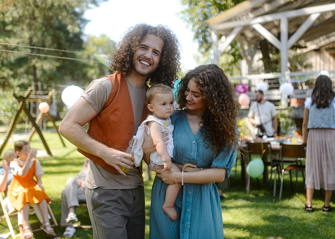 A happy couple pose with their baby at a backyard party.
