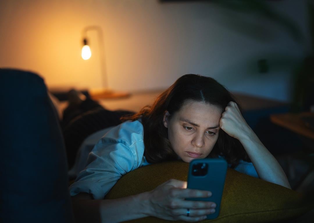 A serious young woman lying on a sofa and scrolling through her phone.