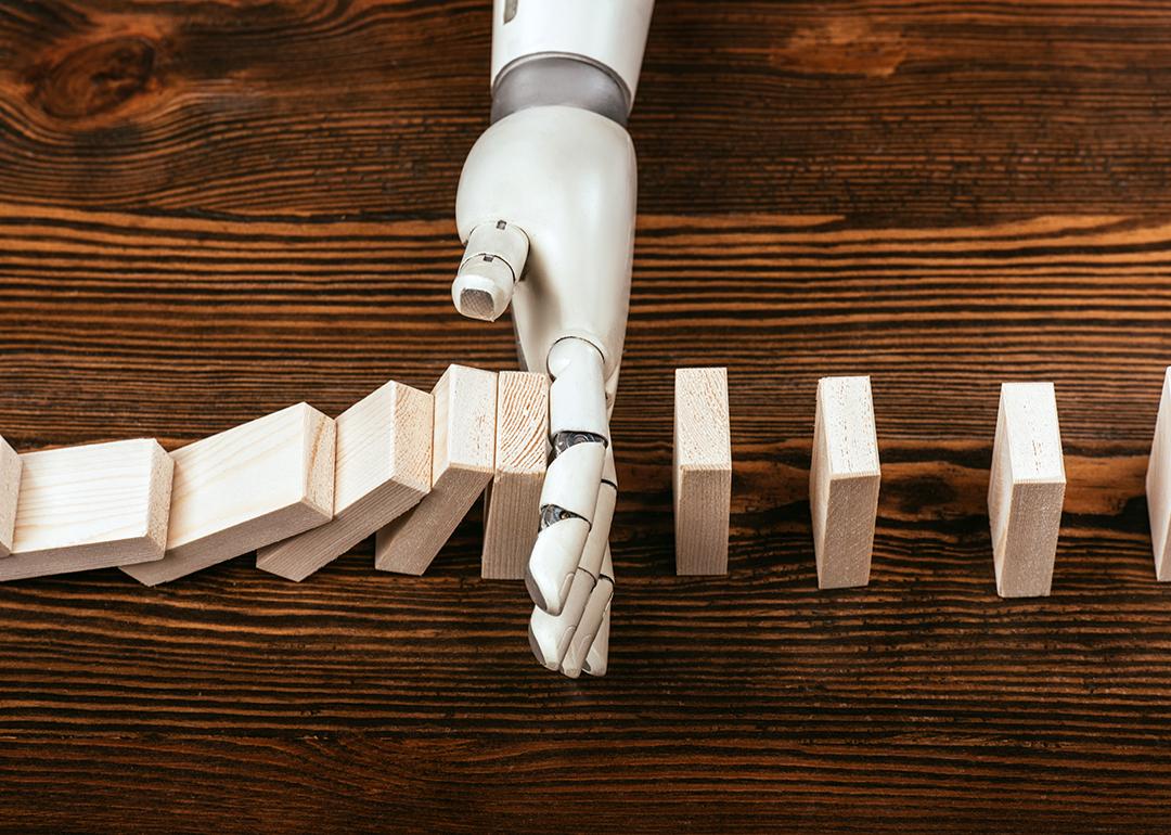 A robotic hand prevents wooden domino blocks from falling midway.
