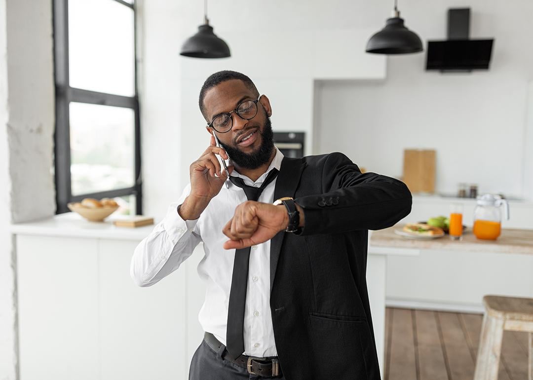 A black businessman on the phone looks at his wrist watch as he gets ready to go to work in the morning.