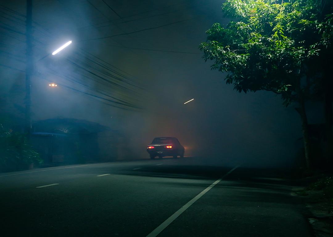 A classic car drives down a spooky road at night.