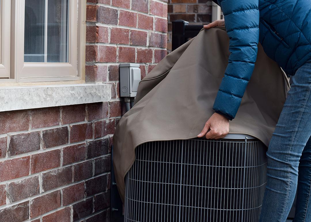 A woman covers their air conditioning unit set outside the house.