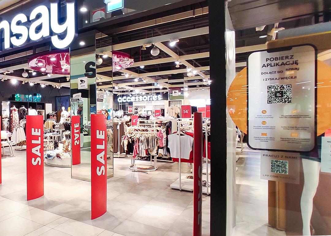 A clothing store having a sale in a shopping mall with a QR code system displayed at the entrance.