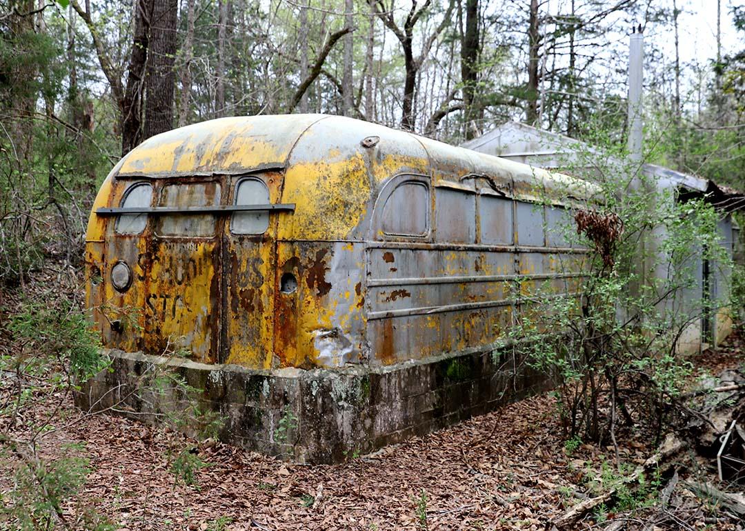 An old, rusty school bus repurposed as an attachment to a shed in the woods.