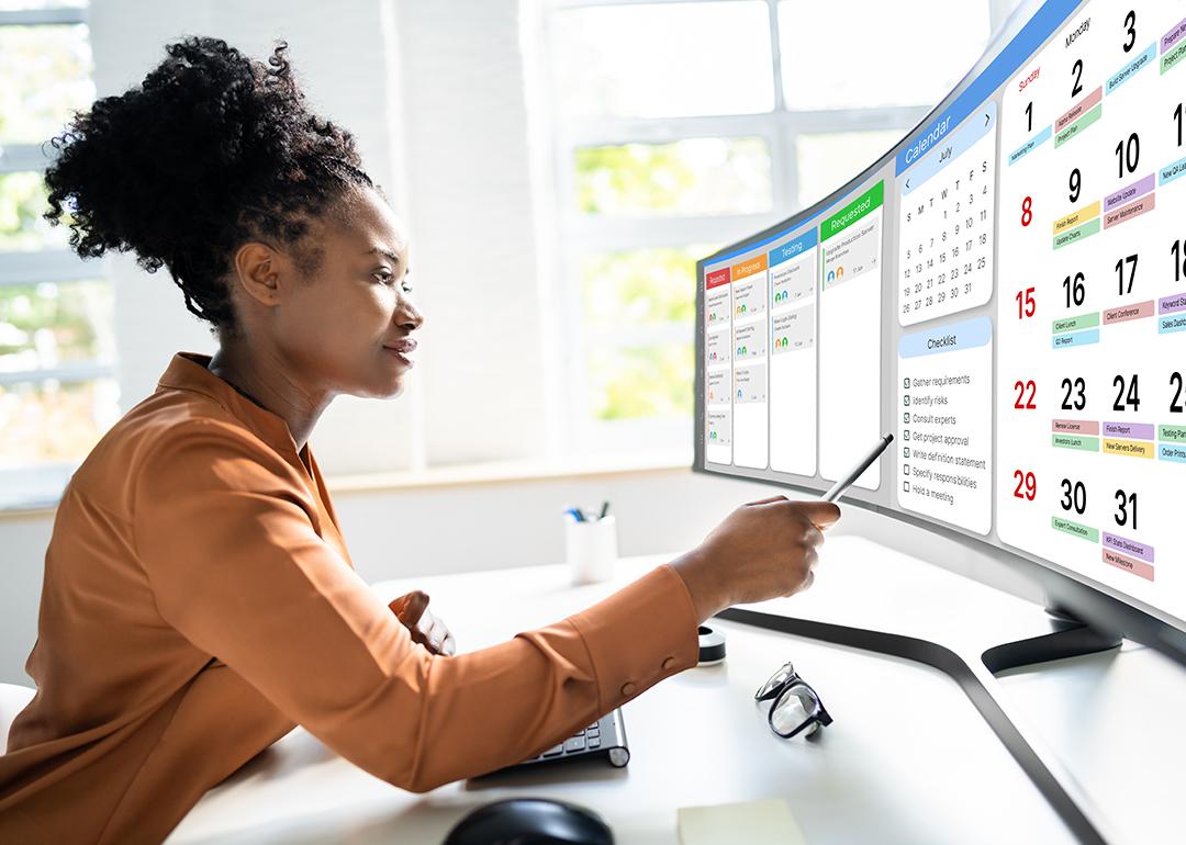 A female project manager uses a digital calendar or scheduling software using a wide monitor in an office.