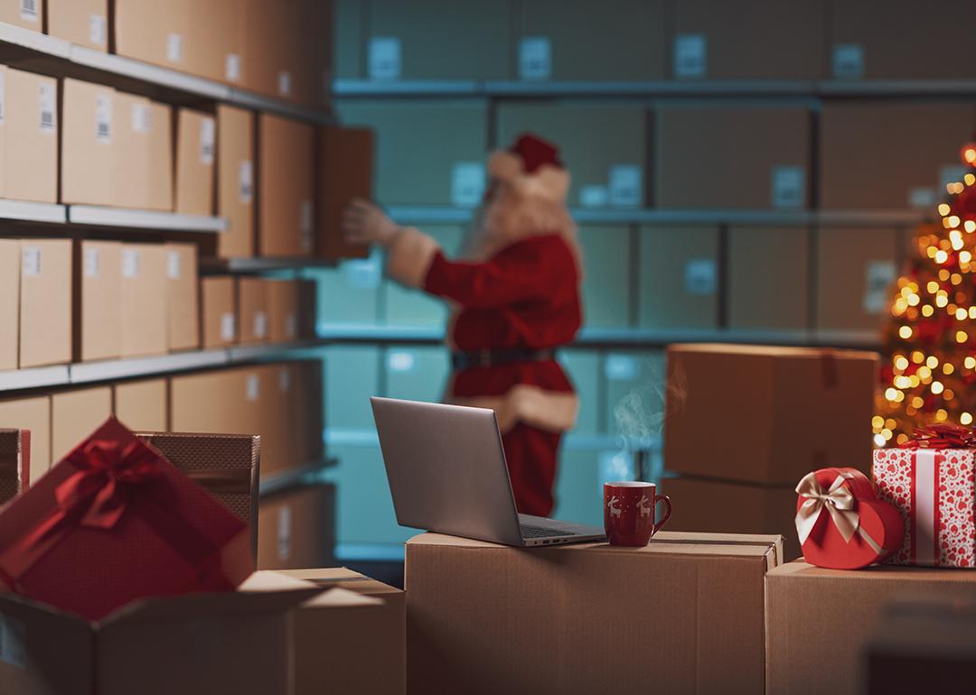 A worker dressed as Santa Claus prepares delivery Christmas gift boxes in a warehouse.