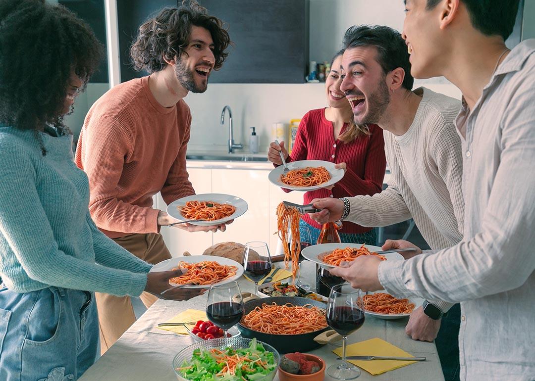 Five people gathered around a table standing with plates full of spaghetti.