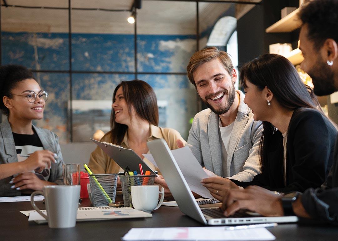 Five members of a business team talking together at a table with laptops open. 