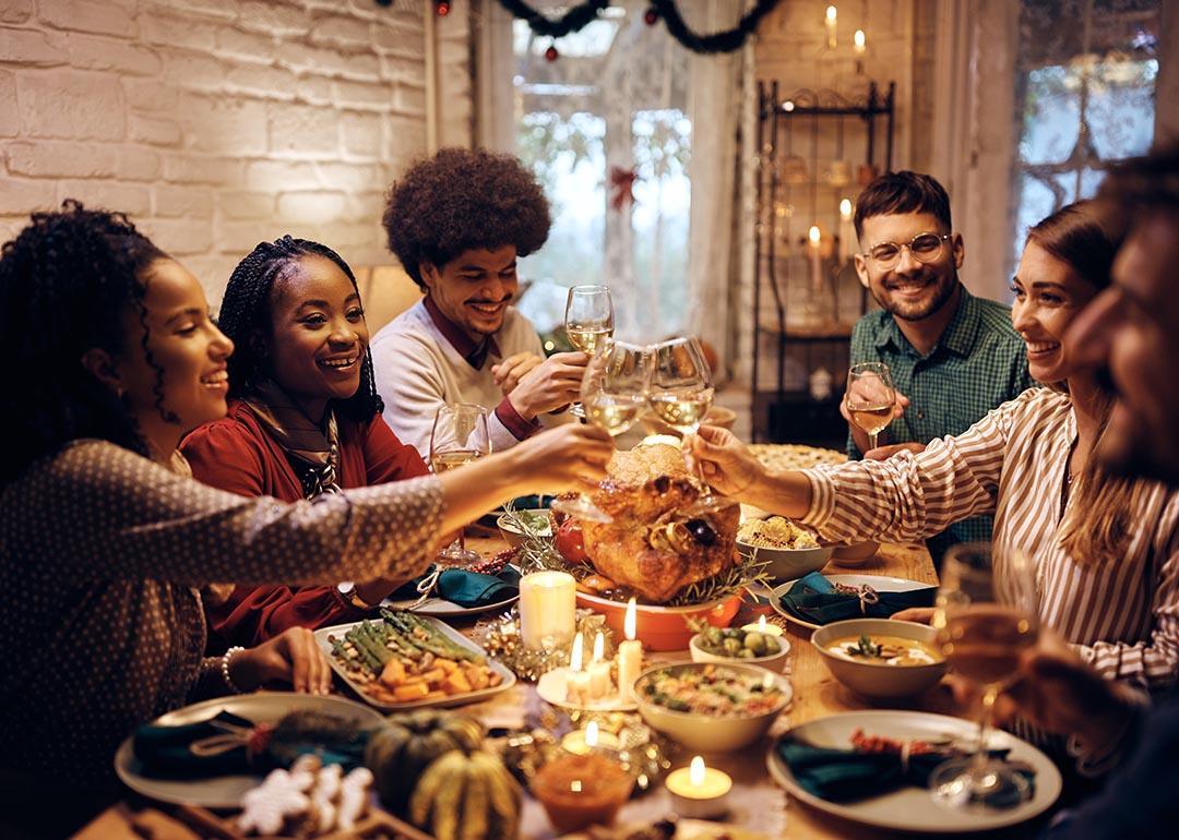 Group of diverse young people toasting at dining table while celebrating Thanksgiving at home.