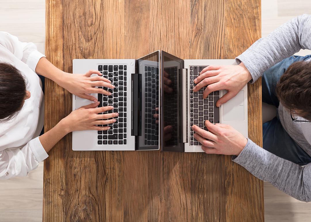 An overhead view of two people using laptops and sitting across each other on a table.