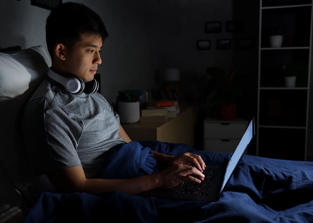 A young man uses his laptop in bed at night.