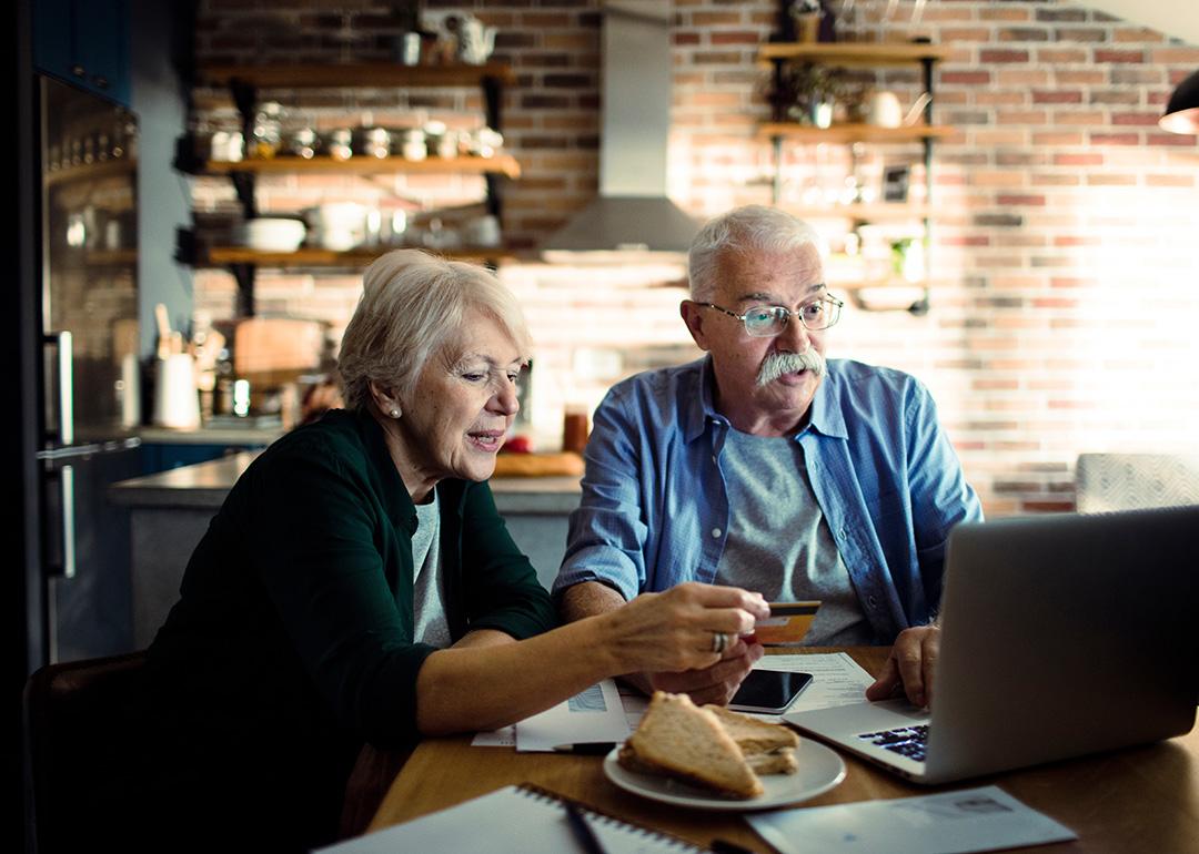 An elderly couple using a credit card at home with a laptop.