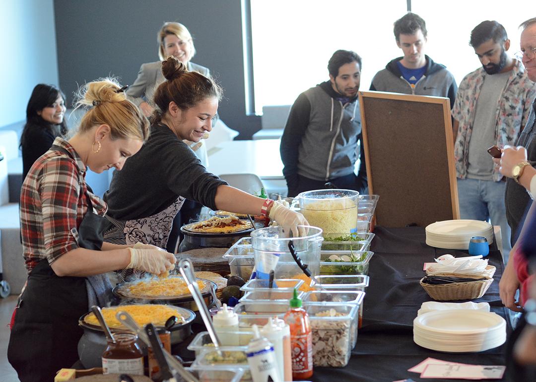 A catering team preparing food in front of awaiting employees.