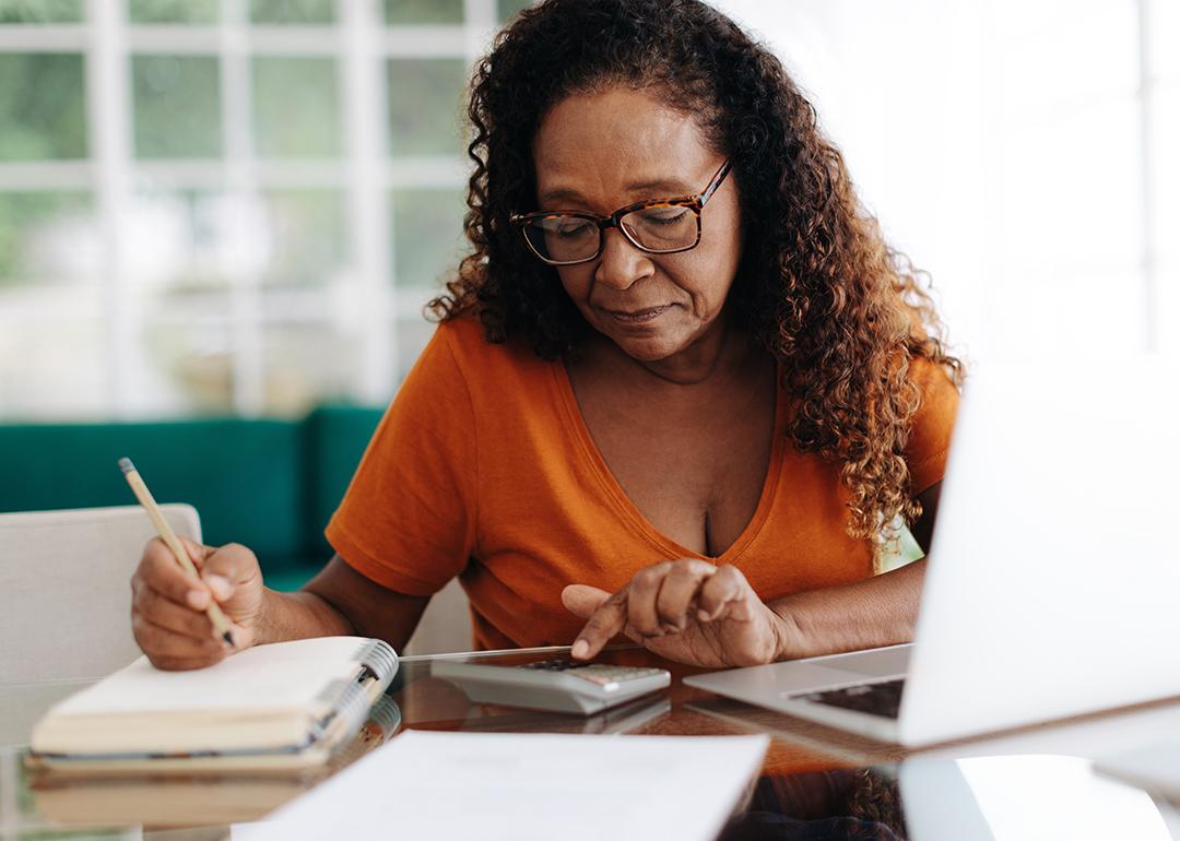 An elderly black woman calculating finances at home.