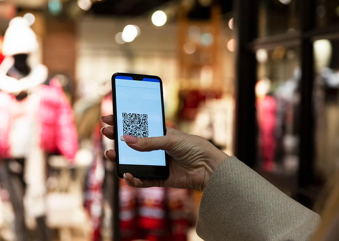 A person scans a QR code in a smartphone in front of a clothing store.