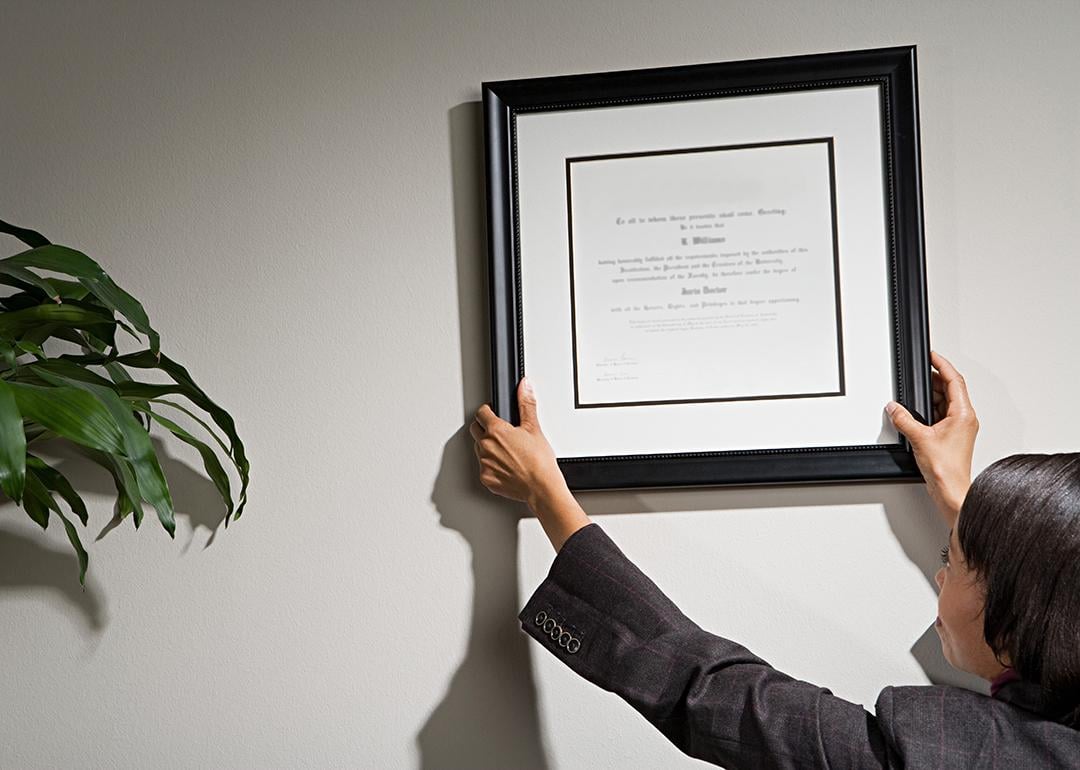 A business woman hanging a framed diploma.