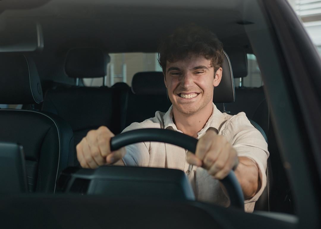 A young man with a big grin sits happily inside a new car.